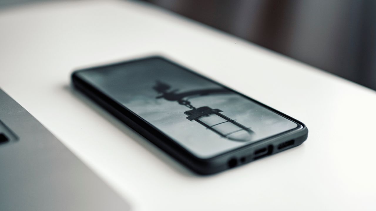 Gros plan d’un smartphone montrant une image floue, posé sur un bureau à côté d’un ordinateur portable.